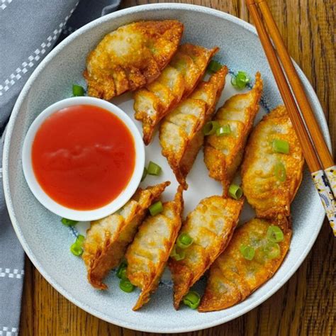 A White Plate Topped With Fried Dumplings Next To A Bowl Of Sauce And