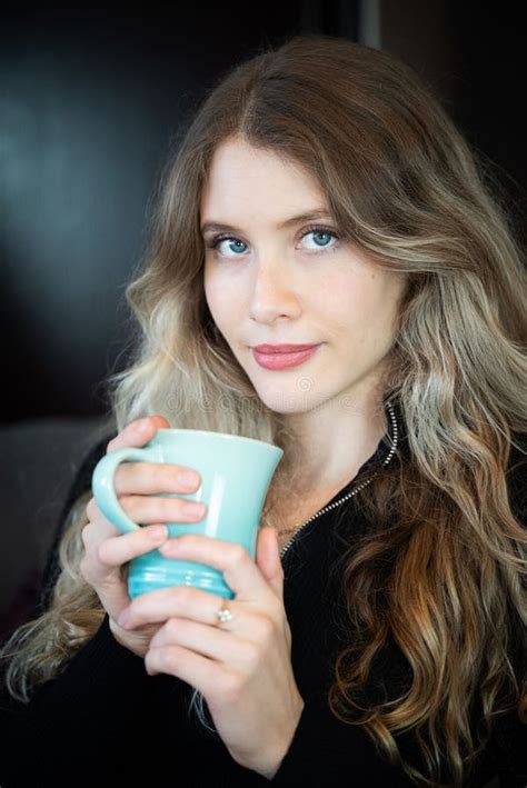 Blonde Woman With Blue Eyes In A Black Top Holding A Blue Cup Stock