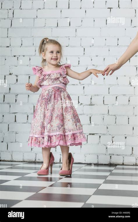 Happy girl in pink dress wearing oversized high heels standing at home ...