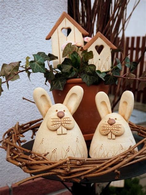 Two White Ceramic Rabbits Sitting In A Bird S Nest Next To A Potted Plant