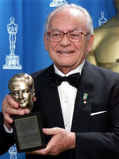 an older man in a tuxedo holding up his award for best supporting actor