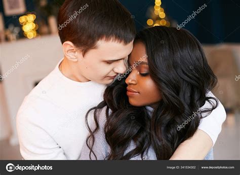 Interracial Loving Young Couple White Guy Hugs A Black Girl Standing In The Room Lights From A