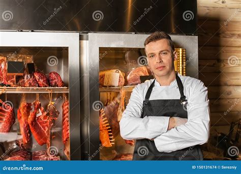 Male Butcher Standing Near Refrigerator With Raw Meat Indoors Stock