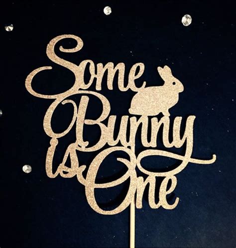 Some Bunny Is One Cake Topper In Gold Glitter On A Black Background