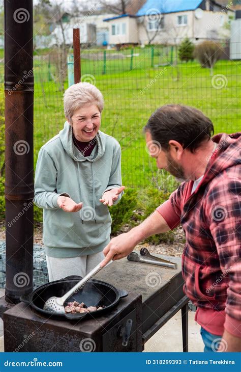 Mature Russian Man And Woman Frying Meat In A Cauldron On The Stove