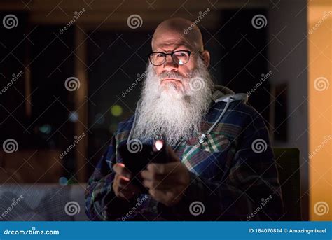 Mature Bald Bearded Hipster Man Thinking While Using Phone At Home In