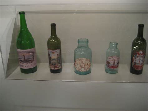 Four Bottles Are Lined Up In A Glass Case On The Shelf Next To Each Other