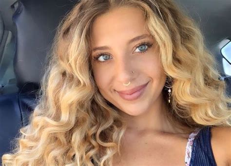 A Woman With Blonde Hair And Blue Eyes Is Smiling In The Back Seat Of A Car