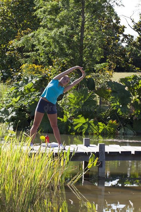 Het Ontspannen Blonde Meisje Uitrekken Zich Op Een Houten Brug En Een Water Stock Afbeelding
