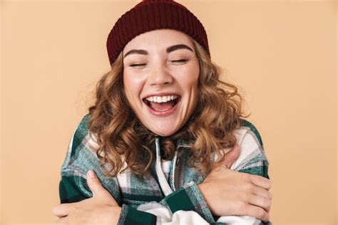 Foto de mujer muy emocionada en gorro de punto abrazándose a sí misma y