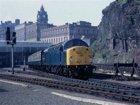 A Yellow And Blue Train Traveling Down Tracks Near A Tall Building With