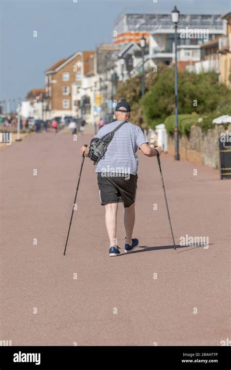 An Old Man Walking Along A Seside Promenade With Two Walking Sticks
