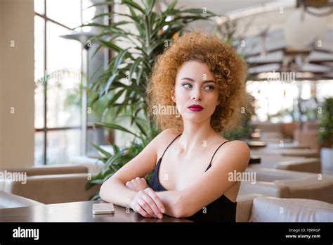 Portrait Of A Young Redhead Woman With Curly Hair Sitting At The Table