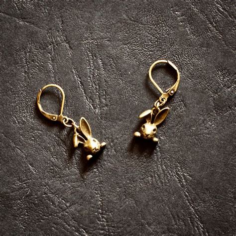 Two Gold Rabbit Earrings On A Black Leather Surface One Is Dangling