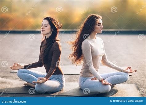 Two Young Women Meditating In Lotus Pose On The Roof Outdoor Stock