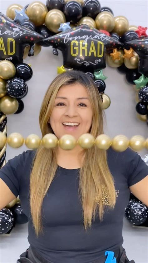 A Woman Is Standing In Front Of Balloons And Garlands That Spell Out Grad