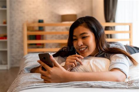 Portrait Of Smiling Young Asian Girl Lying Down On Bed While Making A