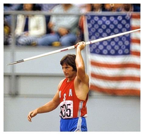 A Man Holding A Pole Above His Head In Front Of An American Flag And Spectators