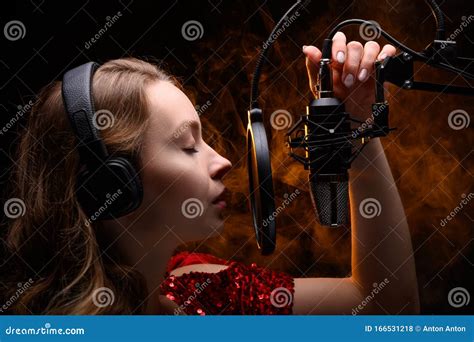 A Vocalist Sings Into A Studio Microphone With Headphones On Her Head