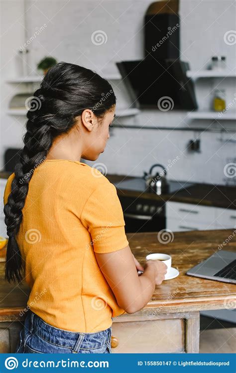 Rear View Of Mixed Race Girl In Orange Shirt Taking Cup Of Coffee Stock