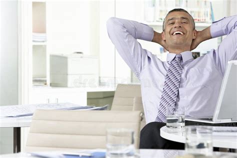 Happy Businessman With Hands Behind Head Looking Up In Office Stock