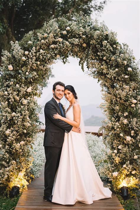 A Bride And Groom Standing In Front Of A Floral Arch