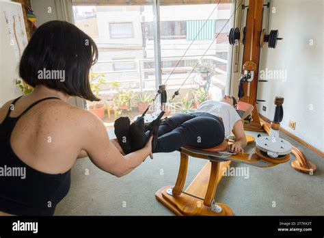 Latina Adult Female Instructor Holding Legs Of Her Female Student Helping Her Do Exercise