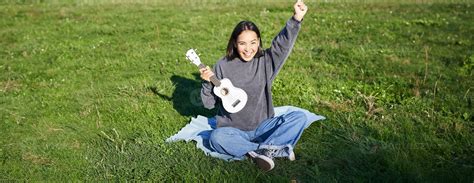 Excited Asian Girl Sits In Park With Ukulele Plays Instrument And