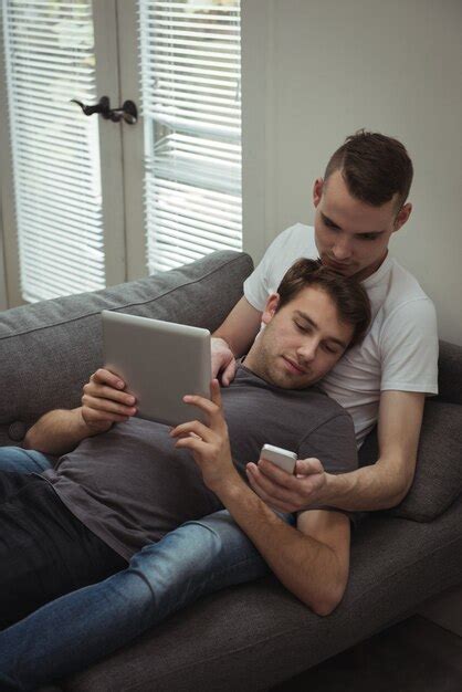 Casal gay usando tablet digital e celular enquanto estava deitado no sofá Foto Grátis