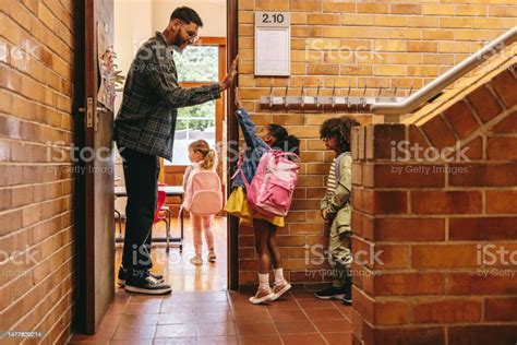 Elementary School Teacher Greeting His Students At The Door Male ...