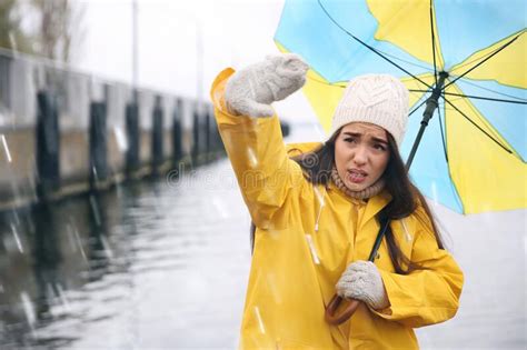 Woman In Yellow Raincoat With Umbrella Caught In Gust Of Wind Near