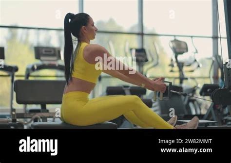 Hispanic Woman Does Exercises On The Rowing Machine A Girl Sits Behind