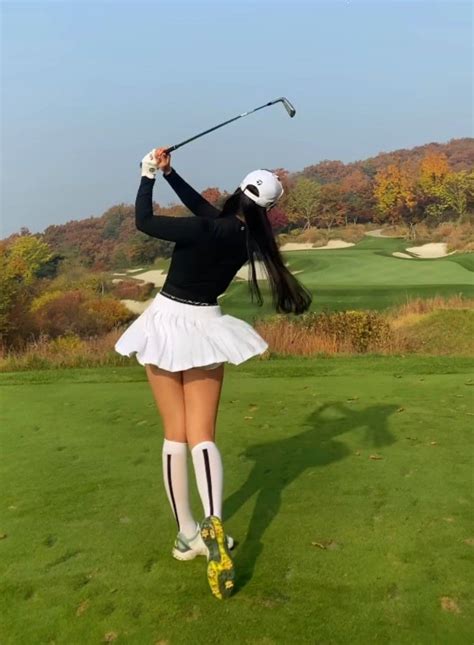 A Woman In A White Skirt And Black Shirt Swinging A Golf Club At The Green