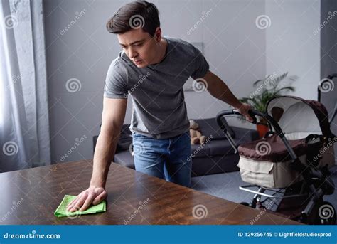 Man Dusting Table With Rag And Holding Pram With Other Hand Stock Image