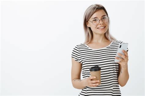 Portrait de jeune fille blonde confiante posant en studio avec son téléphone et son café Photo