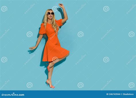 Blonde Frau In Orangefarbenem Cocktailkleid High Heels Und Sonnenbrille Steht Auf Einem Bein