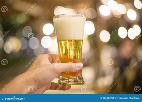 Close Up Of Hand Holding A Glass Of Beer To Celebrate At Restaurant