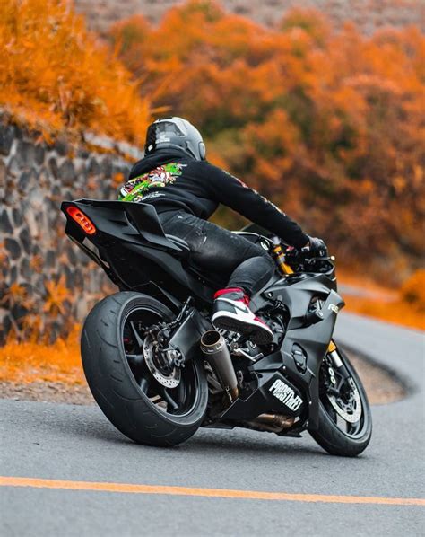 A Man Riding On The Back Of A Black Motorcycle Down A Curvy Road