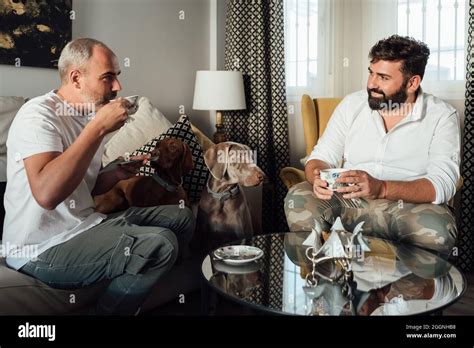 Un couple gay boit du café dans son salon avec ses deux chiens de race Temps de thé à la maison