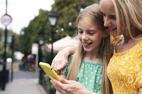 Smiling Mature Woman Sharing Smart Phone With Daughter Stock Photo