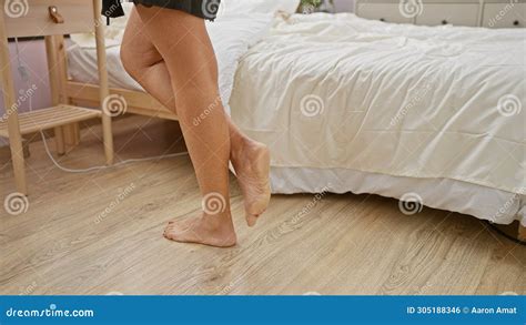 A Woman Standing Barefoot Beside A Bed In A Bedroom With Visible Wooden