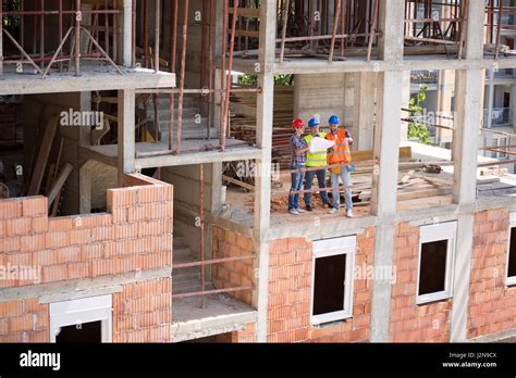 Young Monitoring Team Checking Blue Print On Open Air Building