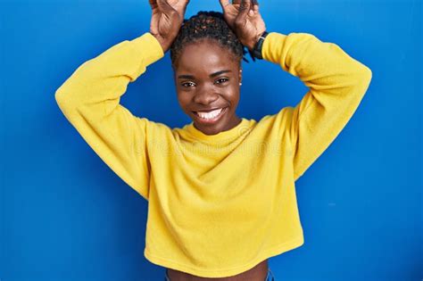 Beautiful Black Woman Standing Over Blue Background Posing Funny And Crazy With Fingers On Head