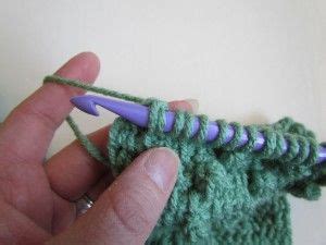 Someone Is Crocheting The End Of A Piece Of Green Yarn With A Purple Needle