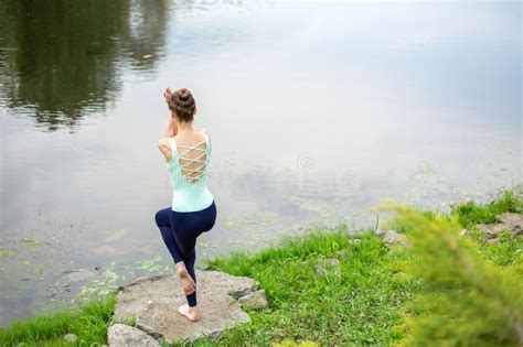 Slim Brunette Girl Doing Yoga In The Summer On A Green Lawn By The Lake