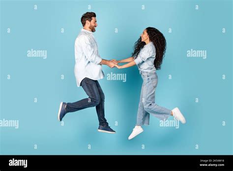 Smiling Millennial Caucasian Male And Arab Lady Holding Hands Jump In