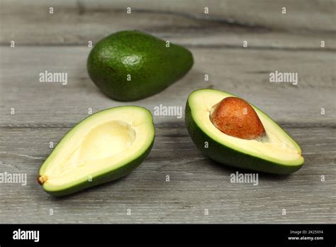 Two Avocados One Cut In Half Seed Visible On Gray Wood Desk Table