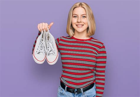 Junge blonde Frau mit weißen Freizeitschuhen sieht positiv und