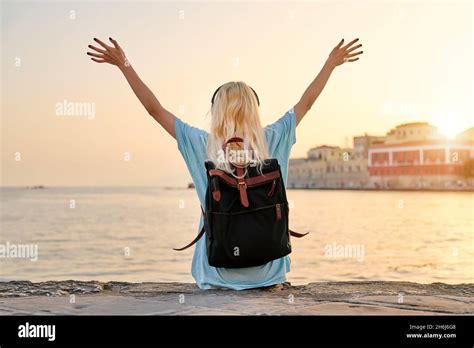 Back View Blonde Woman In Headphones With Backpack Sitting On City Sea