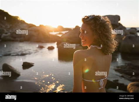 Woman Standing At Rocky Seaside Beach During Golden Hour Wearing White Bikini Top And